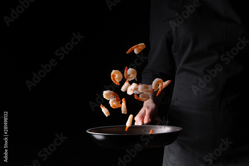 Seafood, chef prepares shrimps in a frying pan, roasts. On a black background for design, menus, restaurants, oriental cuisine, healthy food. Horizontal photo, banner