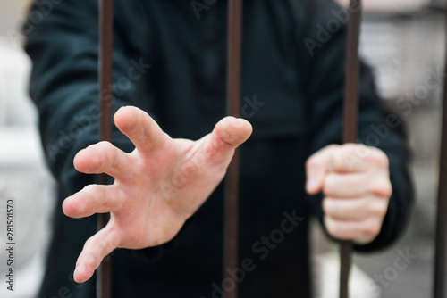 Man's hand stretches through the bars locked man in a cage cell. Hand of a refugee behind fence