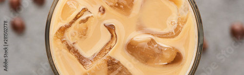 close up view of ice coffee in glass with straw and coffee grains on grey background, panoramic shot