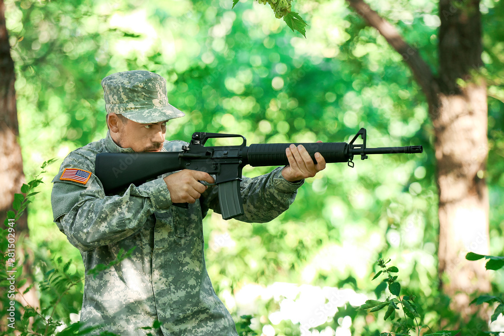 Fototapeta premium Soldier in camouflage taking aim in forest