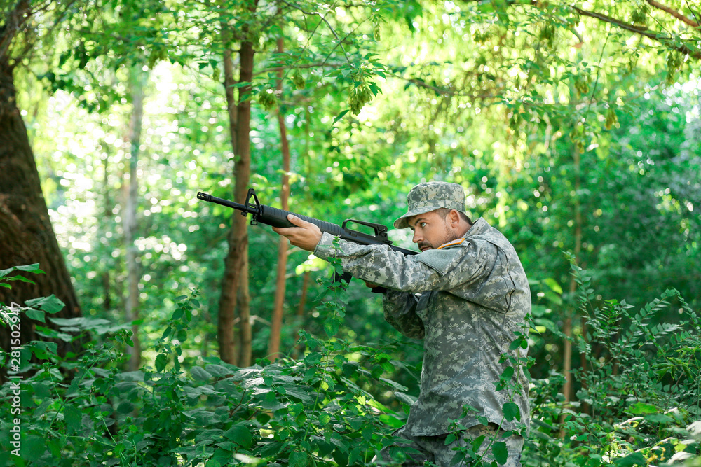 Obraz premium Soldier in camouflage taking aim in forest