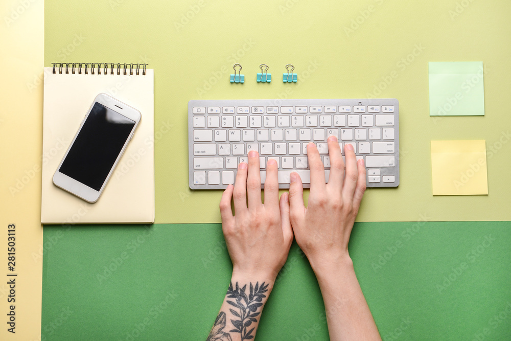 Female hands with PC keyboard, mobile phone and stationery on color background Female hands with PC keyboard, mobile phone and stationery on color background