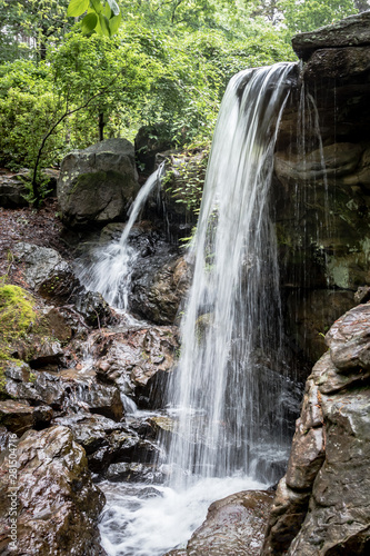 Two waterfalls, one tall and one short cascading over a rocky ledge.