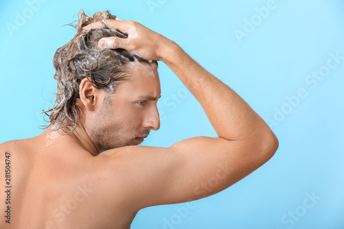Handsome young man washing hair against color background