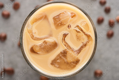 close up view of ice coffee in glass with straw and coffee grains on grey background