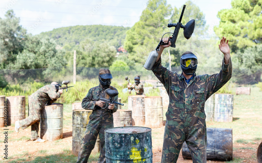 Fototapeta premium Poddał się gracz paintballu w ochronnej formie i masce z rozchlapywaną farbą stojącą z podniesionymi rękami