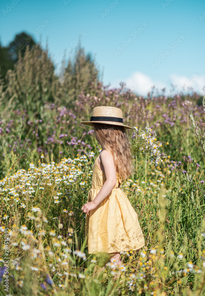 Cute little girl walking in the flowers field in yellow dress and hat ...