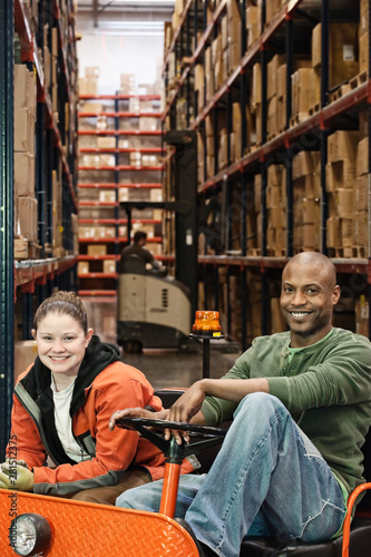 Portrait of smiling workers sitting in motorized cart in warehouse