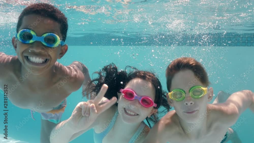 happy children swimming underwater in pool smiling waving hands children enjoying swim floating together in crystal clear water on summer vacation