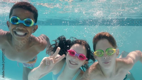 happy children swimming underwater in pool smiling waving hands children enjoying swim floating together in crystal clear water on summer vacation