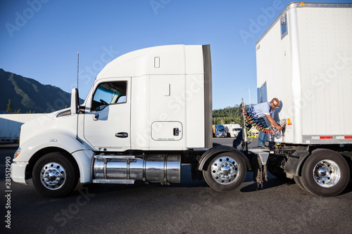 Man attaching power cable from truck tractor to trailer at truck stop