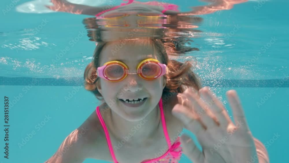 happy little girl swimming underwater in pool smiling waving hand