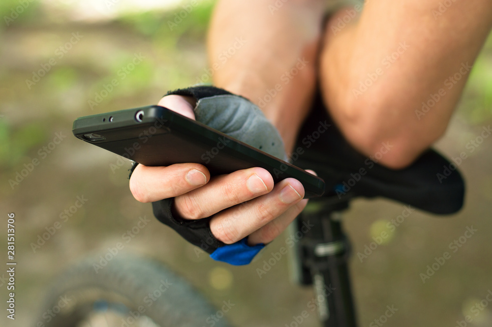 A cyclist in gloves checks the route on the phone. Close-up, in nature. Sports break in the journey.