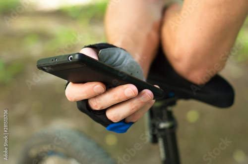 A cyclist in gloves checks the route on the phone. Close-up, in nature. Sports break in the journey.