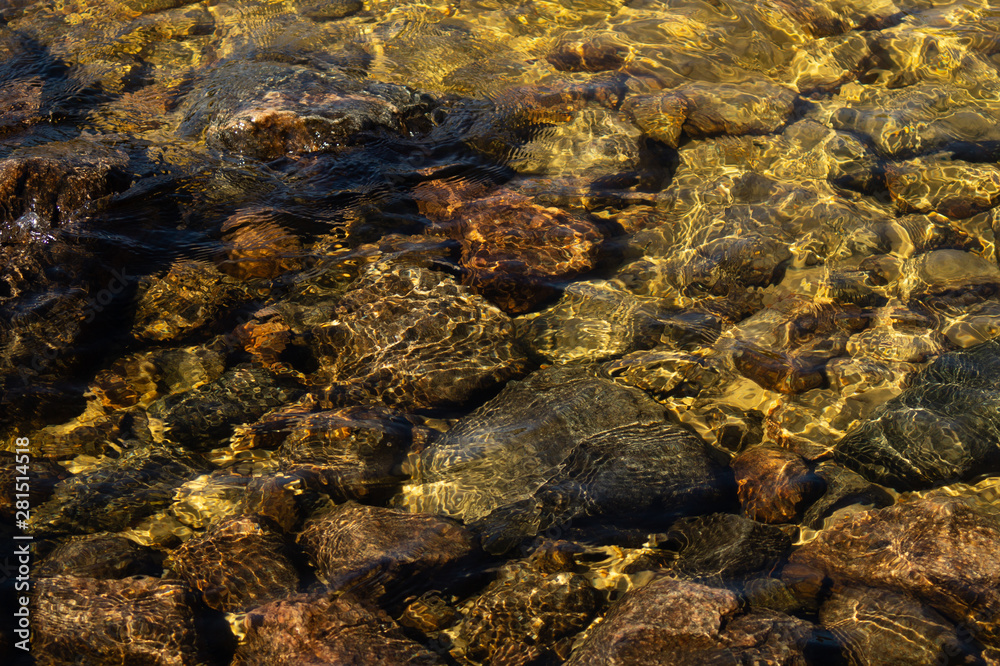 Shiny transparent water. clear water with pebbles and stone on the bottom. shining reflections of sun rays and ripples on the water