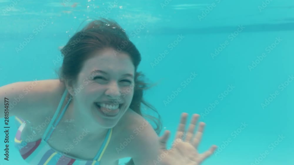 Beautiful Woman Swimming Underwater In Pool Smiling Waving Hand Floating In Blue Crystal Clear