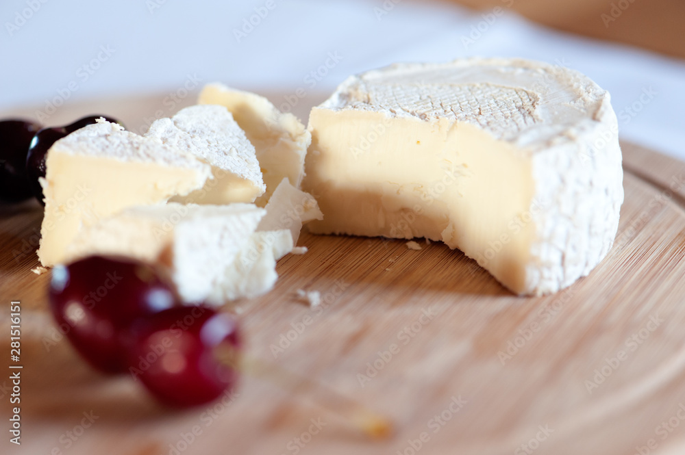 Camembert from goat's milk cut into slices on a wooden board still life with sweet cherry berries close-up
