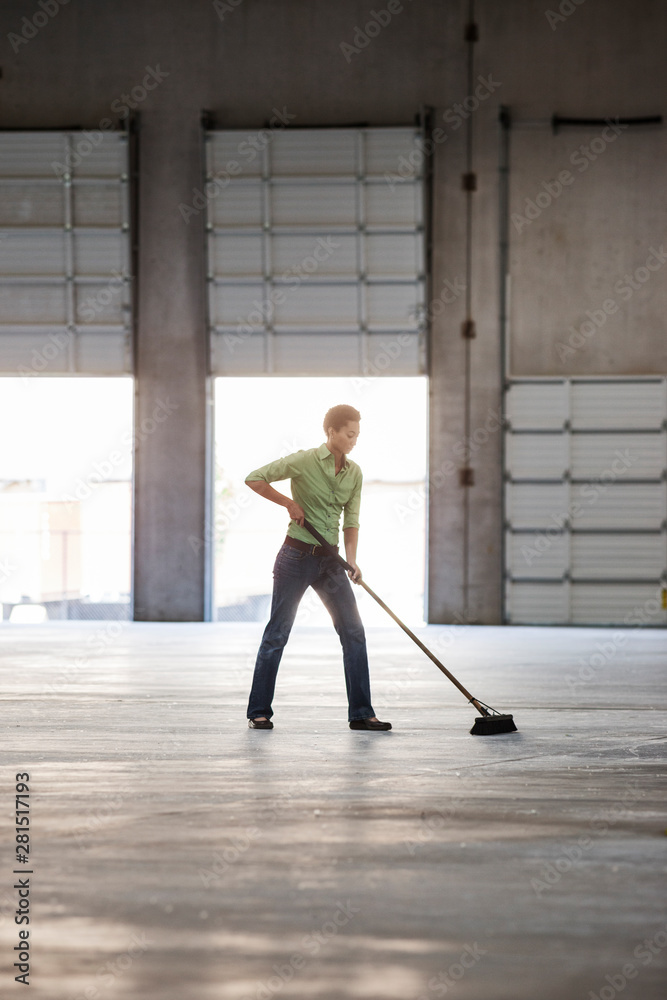 © Mint Images - Woman sweeping up in warehouse