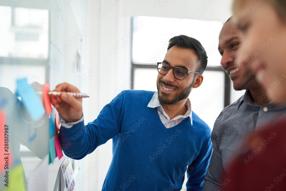 Obraz premium Portrait of an indian man in a diverse team of creative millennial coworkers in a startup brainstorming strategies