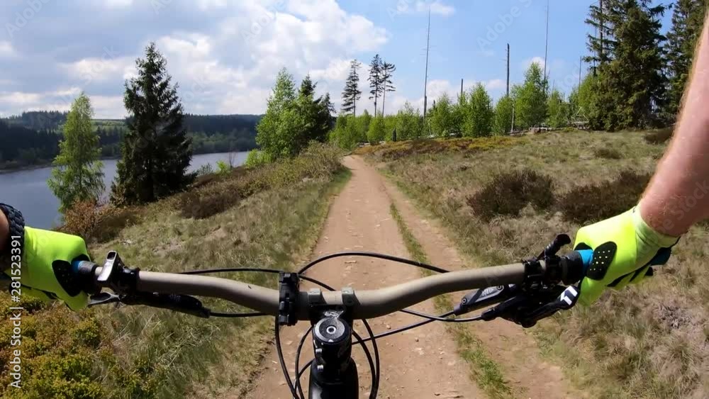 First person view of a mountain biker riding trails on a sunny day with a Canyon Strive Enduro bike in the Harz region in Germany with a beautiful lake on the left, filmed with GoPro Hero 7 in 4K. First person view of a mountain biker riding trails on a sunny day with a Canyon Strive Enduro bike in the Harz region in Germany with a beautiful lake on the left, filmed with GoPro Hero 7 in 4K.