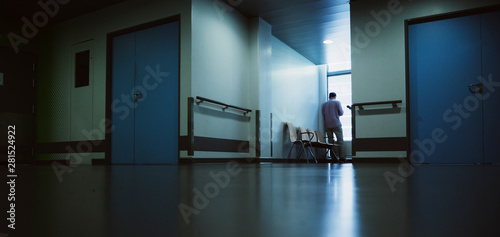 Lonely patient in full length in modern hospital waiting lobby room near the window as he waits for good or bad news from his doctor - blue hospital atmosphere photo