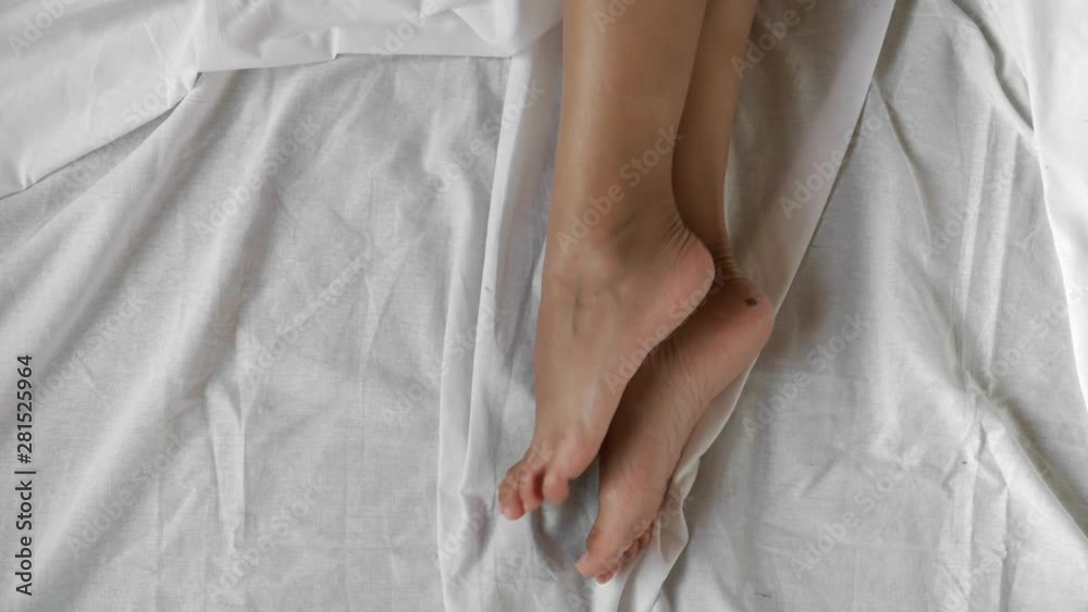Top view, close-up. Beautiful female legs twist gracefully in bed on a white sheet. Top view, close-up. Beautiful female legs twist gracefully in bed on a white sheet.