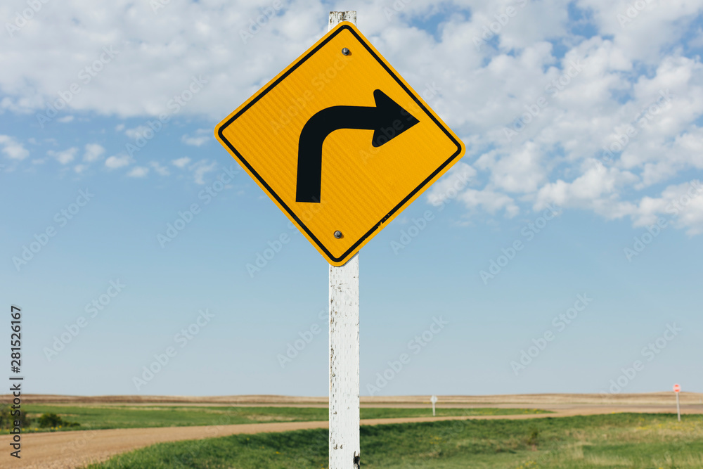 Close up of caution turn ahead sign against cloudy sky Close up of caution turn ahead sign against cloudy sky