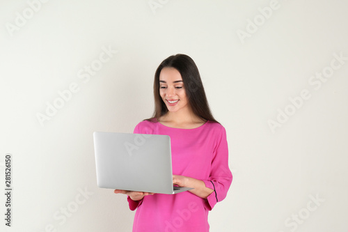 Portrait of young woman in casual outfit with laptop on light background