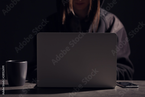 Woman with laptop and smartphone at table in darkness, closeup