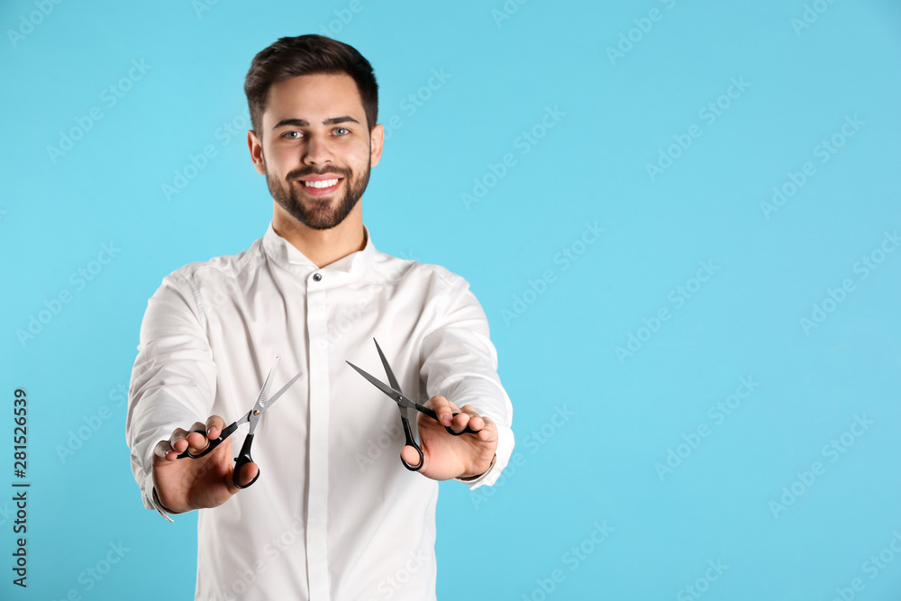 Fototapeta premium Young hairstylist holding professional scissors on color background, space for text