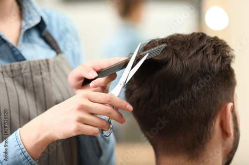 Barber making stylish haircut with professional scissors in beauty salon, closeup