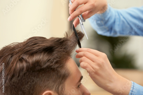 Barber making stylish haircut with professional scissors in beauty salon, closeup