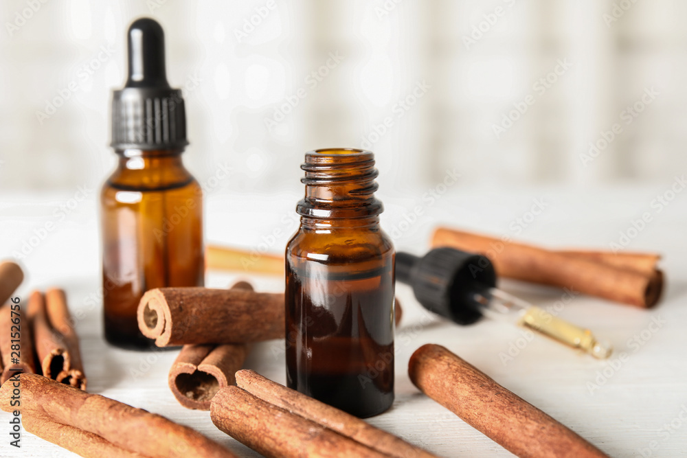 Bottles of essential oils and cinnamon sticks on white wooden table