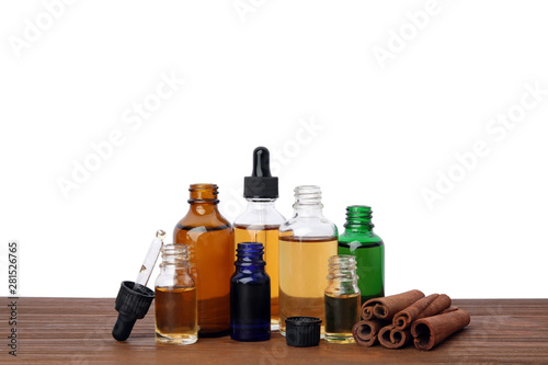 Bottles of essential oils and cinnamon sticks on wooden table against white background