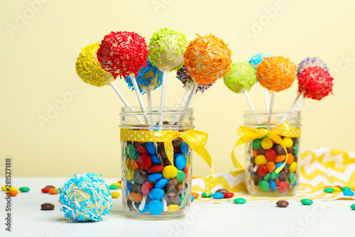 Glass jars with tasty cake pops and dragee on table against yellow background