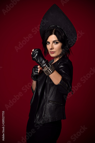 Young stylish brutal woman brunette in neofolk clothes stands in a fighting stance ready to punch on dark red