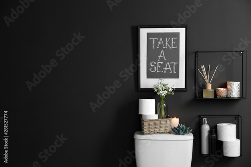 Decor elements, necessities and toilet bowl near black wall, space for text. Bathroom interior