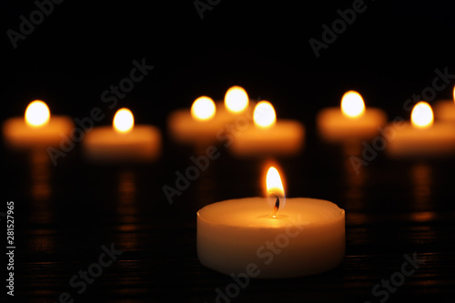 Burning candle on black table against blurred background  space for text