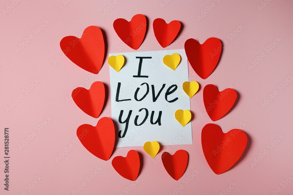 Frame made of paper hearts and card with phrase I LOVE YOU on pink background, flat lay