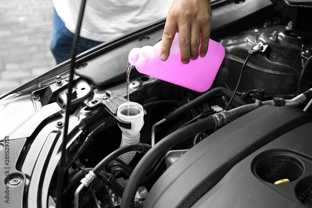 Man pouring liquid from plastic canister into car washer fluid reservoir, closeup Man pouring liquid from plastic canister into car washer fluid reservoir, closeup