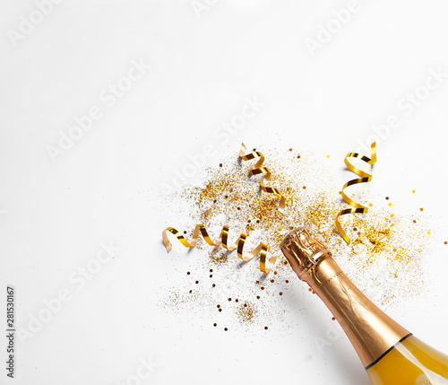 Photo Bottle of champagne with gold glitter, confetti and space for text on white background, top view