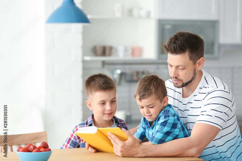 Dad and his sons reading interesting book in kitchen. Space for text Dad and his sons reading interesting book in kitchen. Space for text