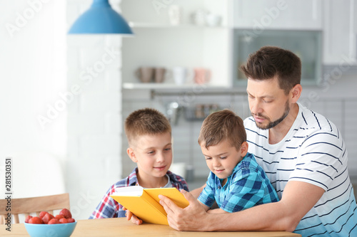 Dad and his sons reading interesting book in kitchen. Space for text