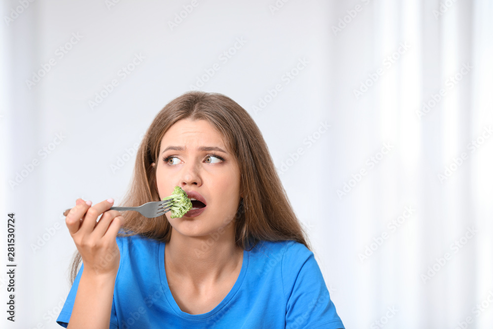 Portrait of unhappy woman eating broccoli on light background Portrait of unhappy woman eating broccoli on light background