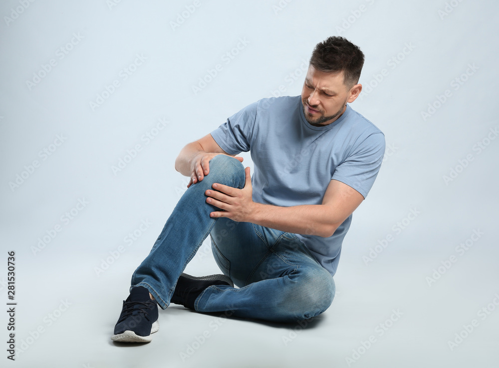 Full length portrait of man with knee problems sitting on grey background Full length portrait of man with knee problems sitting on grey background