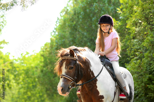 Obraz na plátně Cute little girl riding pony in green park