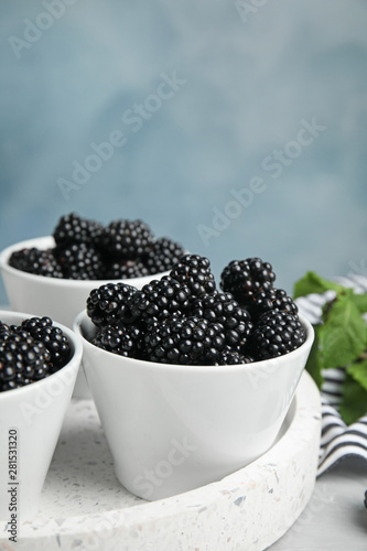 Tray with bowls of tasty blackberries on grey marble table against blue background