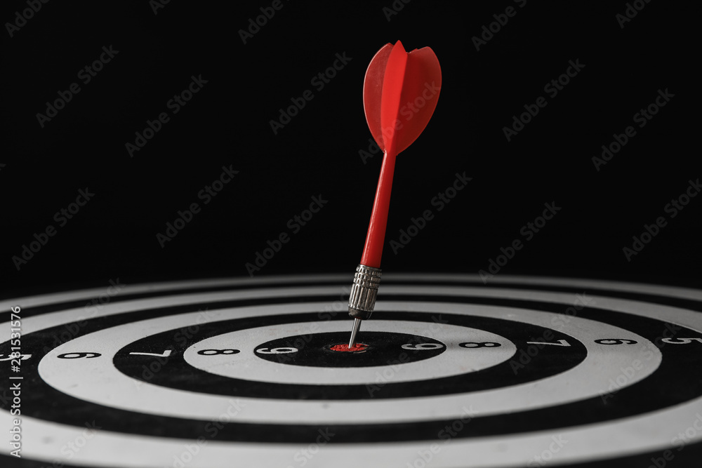 Red arrow hitting target on dart board against black background Red arrow hitting target on dart board against black background