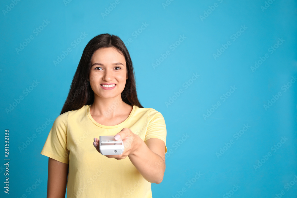 Happy young woman operating air conditioner with remote control on light blue background. Space for text Happy young woman operating air conditioner with remote control on light blue background. Space for text
