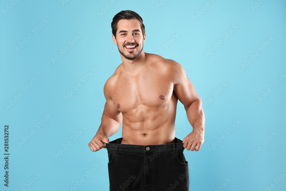 Young man with slim body in old big size jeans on light blue background